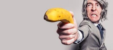 mand med paryk angriber med en banan der skal forestille en pistol